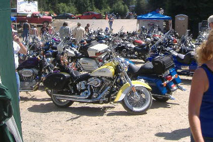 Parking lot filled with motorcycles and a few people.