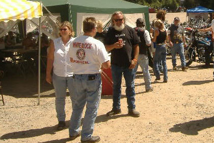 Group of people talking outside of a tent surrounded by motorcycles.