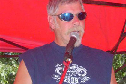 Man speaks through microphone under bright red tent.