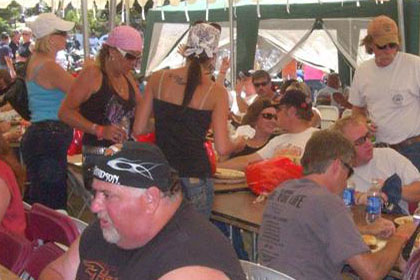 Long tables under a tent filled with people eating and talking.