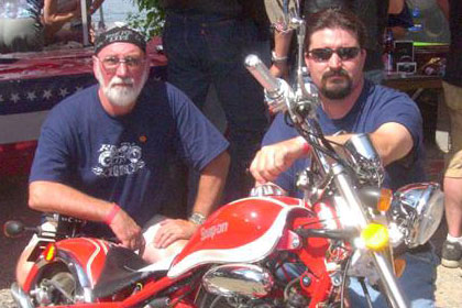 Two men pose with motorcycle.