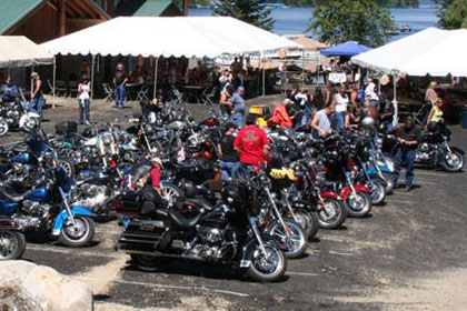 Lots of motorcycles fill parking lot outside of event venue.