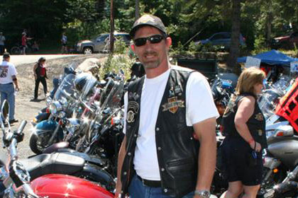 Man poses in front of a red motorcycle. Lots of other motorcycles in background.