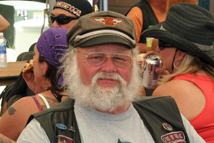 Man smiles for camera. Lots of other people surround him at tables.