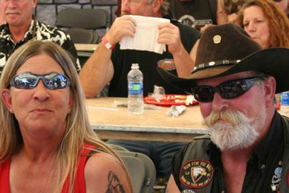 Couple smiles for camera. People sit at tables in background.