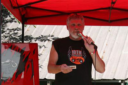Man speaks through microphone under bright red tent.