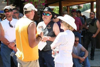 People stand in groups at event in front of large wood and stone building.