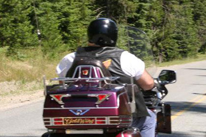 Two lines of motorcycles on road driving away from camera and towards lake in distance.