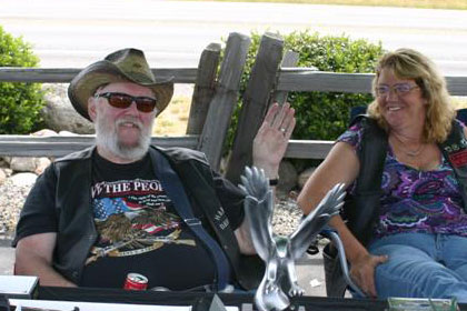 Man and woman sit in chairs behind table full of knives.