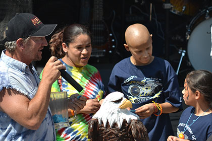 Man speaking on a microphone next to a group of children.