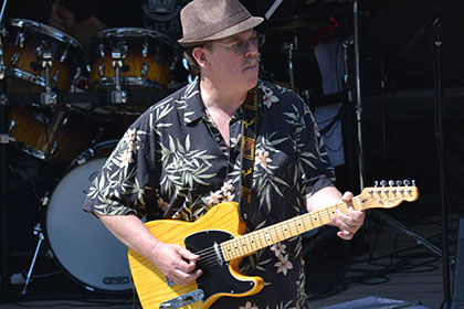 Man wearing a hat plays guitar on stage.