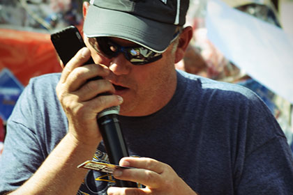 Man wearing a hat and sunglasses speaks on the microphone.
