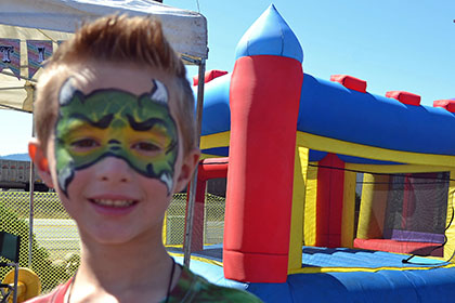 Child with painted face stands in front of a bouncy castle.