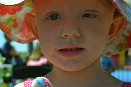 Child wearing a hat and holding a stuffed animal.