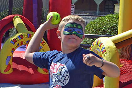 Child with a painted face throws a ball at the dunk tank.