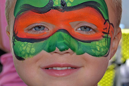 Child with their face painted like a Ninja Turtle.