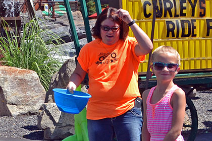 Man falls into the water in the dunk tank while a Ride for Life volunteer stands next to a child.