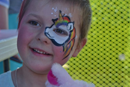 Child witha painted face holds a stuffed animal.