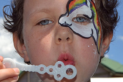 Child with a painted face blowing bubbles.