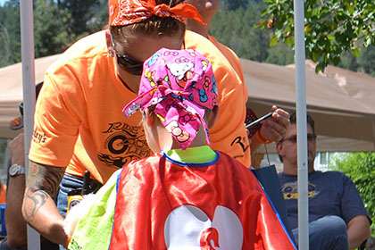 Ride for Life volunteer helping a child wearing a red cape and pink bandana.