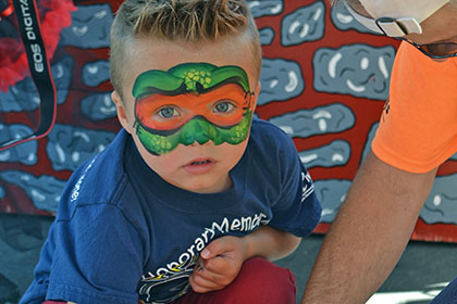 Child with a painted face grabs items from a red basket.