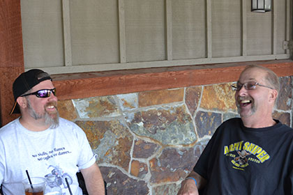 Couple guys laughing while sitting at a table outside.