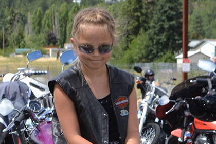 Child sitting upon a large rock next to the motorcycles in the parking lot.