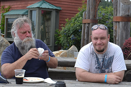 Two men sitting at a wooden table outside.