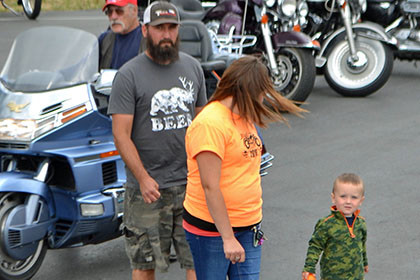 A bearded man, Ride for Life volunteer, and child walk in the parking lot.