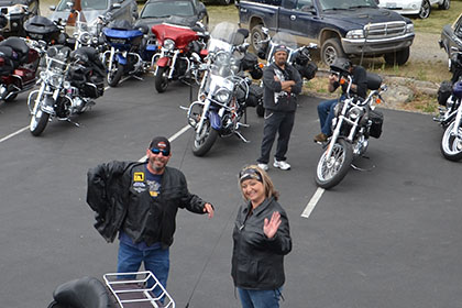 Motorcycles, vehicles, and people in the parking lot.l