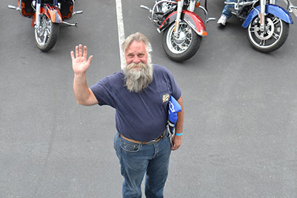 Bearded man in the parking lot, waving to the camera.