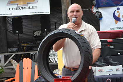 Man on microphone standing behind a motorcycle tire and motorcycle lift.