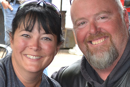 Man and woman smiling for camera while sitting at an outside table.