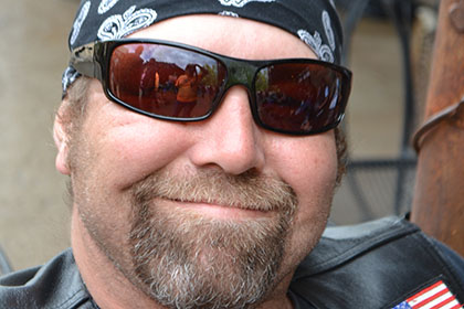 Man wearing sunglasses and bandana smiles for the camera.