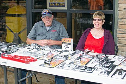 Man and woman sitting at their booth outside with many items on their table.
