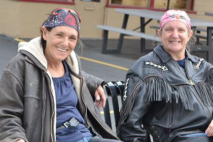 Two people wearing bandana sit on a bench outside.