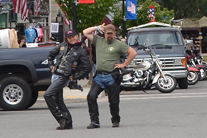 Two people pose for the camera while others gather next to their motorcycles.