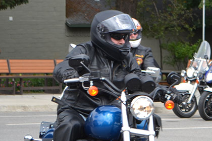 Rider driving their motorcycle while other riders sit on their parked motorcycles.