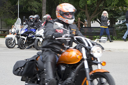 Rider driving their motorcycle while other riders sit on their parked motorcycles.