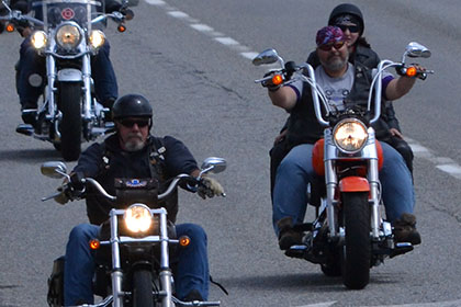 Four riders and a white vehicle on the road.