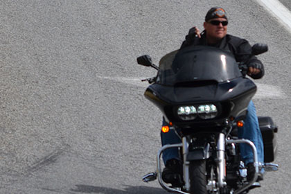 Two people ride their motorcylces while a person dressed as a Minion stands on the road.